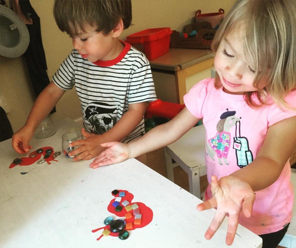 Two children making crafts with red cutouts and small colorful objects