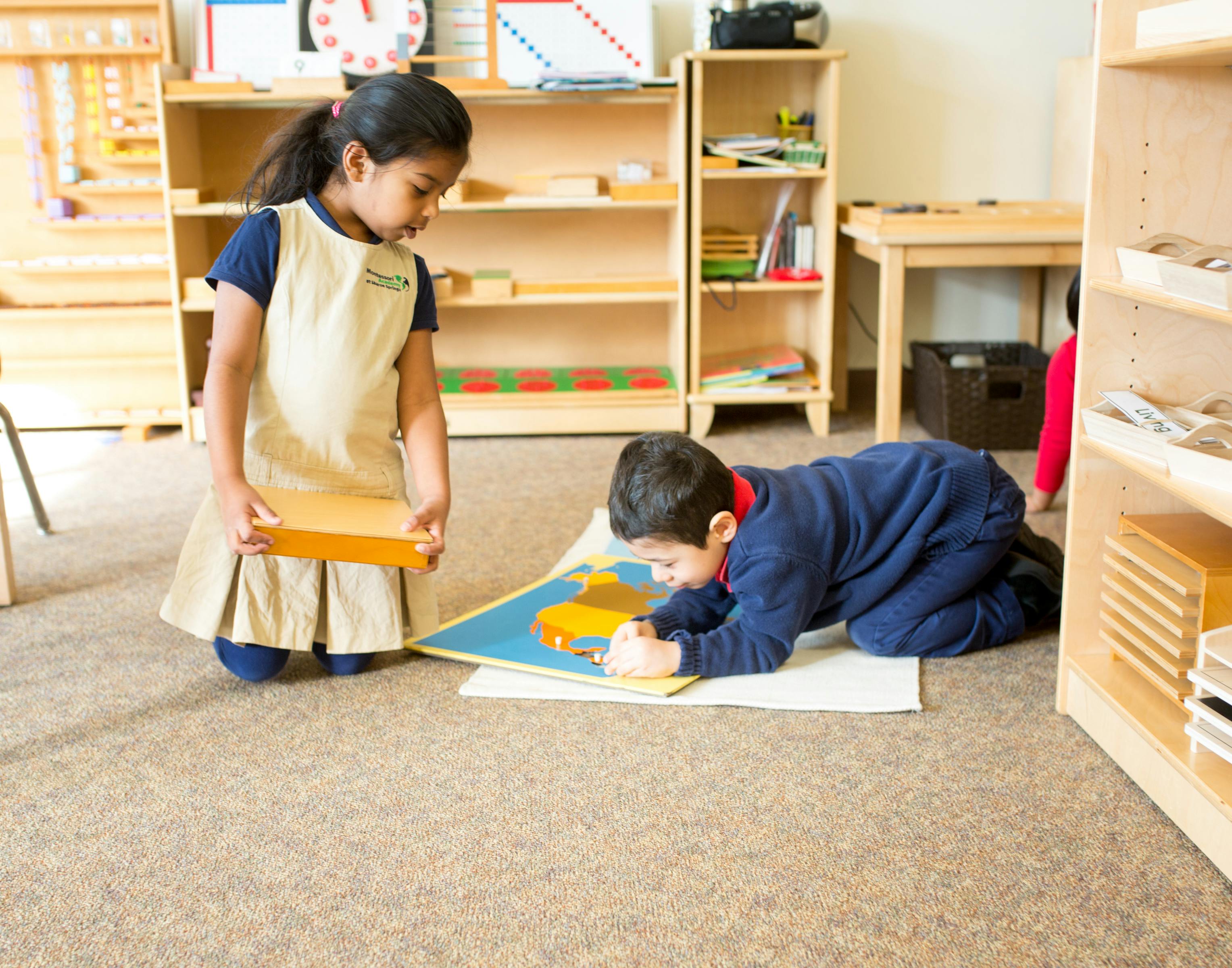 Child holding a wooden block while another child draws on the floor