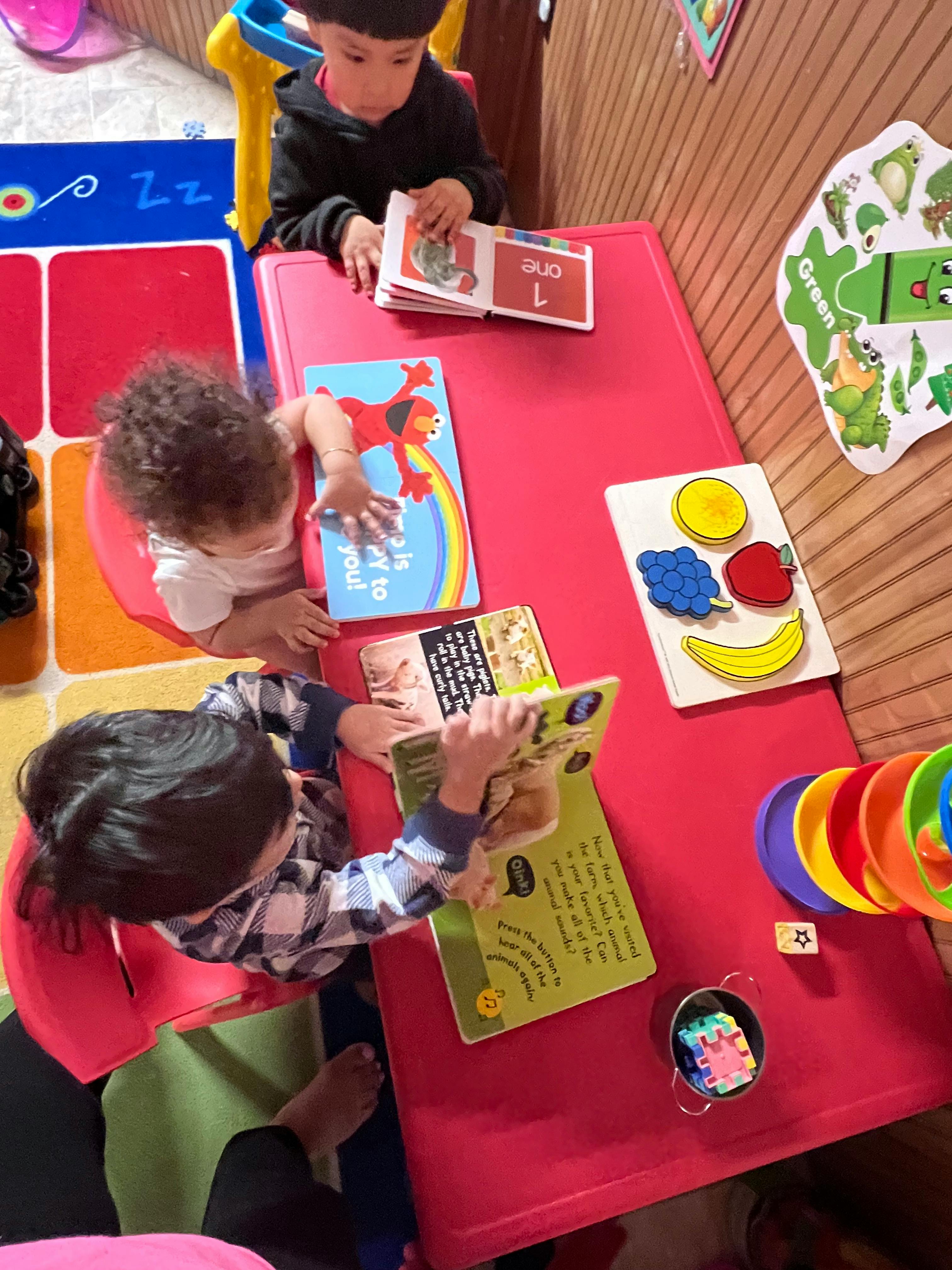 Three children reading books at a red table