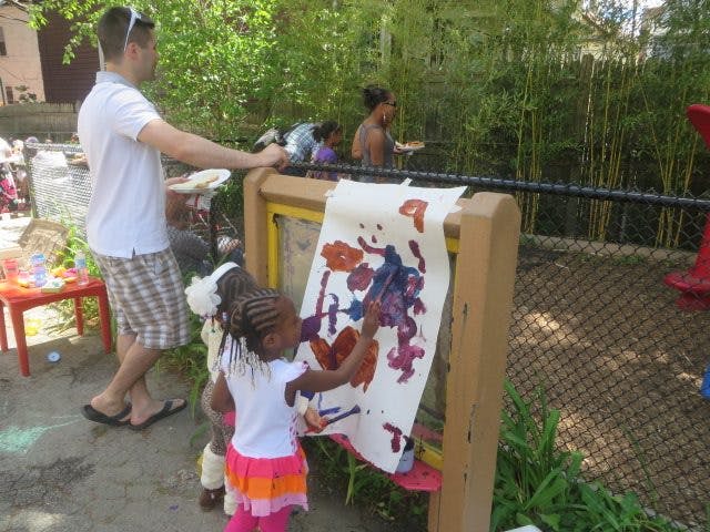 Child painting on an easel outdoors with an adult standing nearby