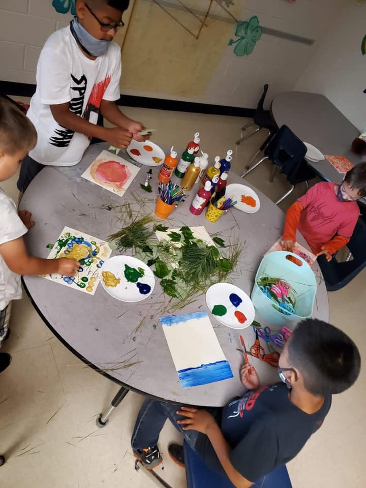 Children painting at a table with leaves and paint bottles