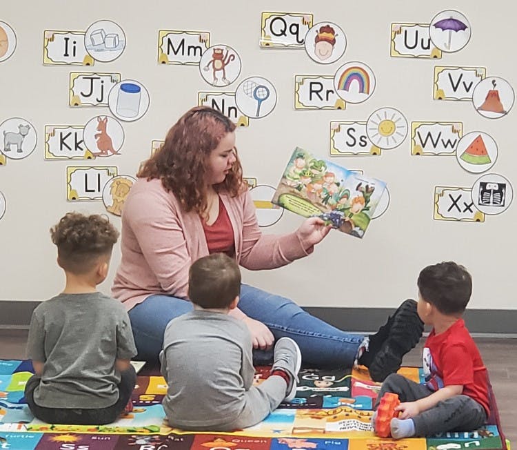 Person reading a book to three children in a classroom