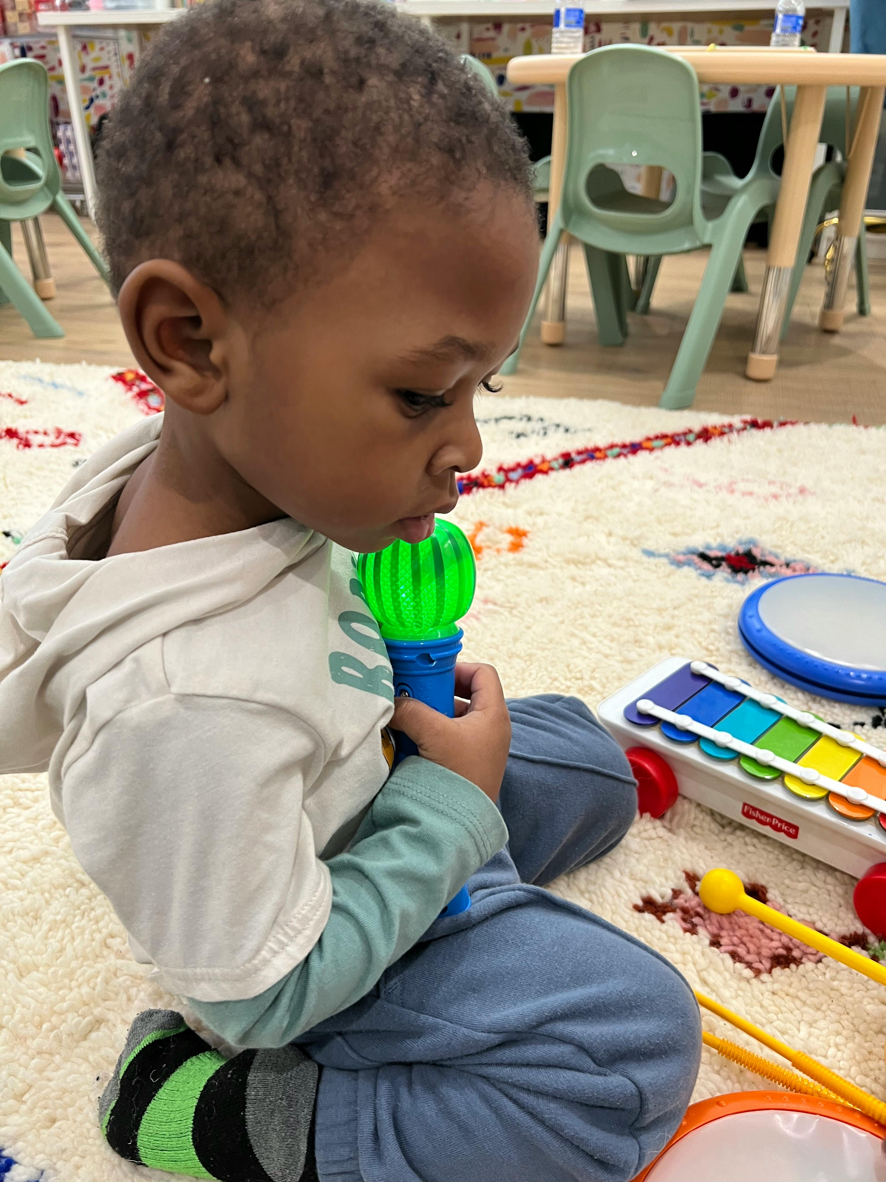 Child sitting on a rug holding a green and blue toy
