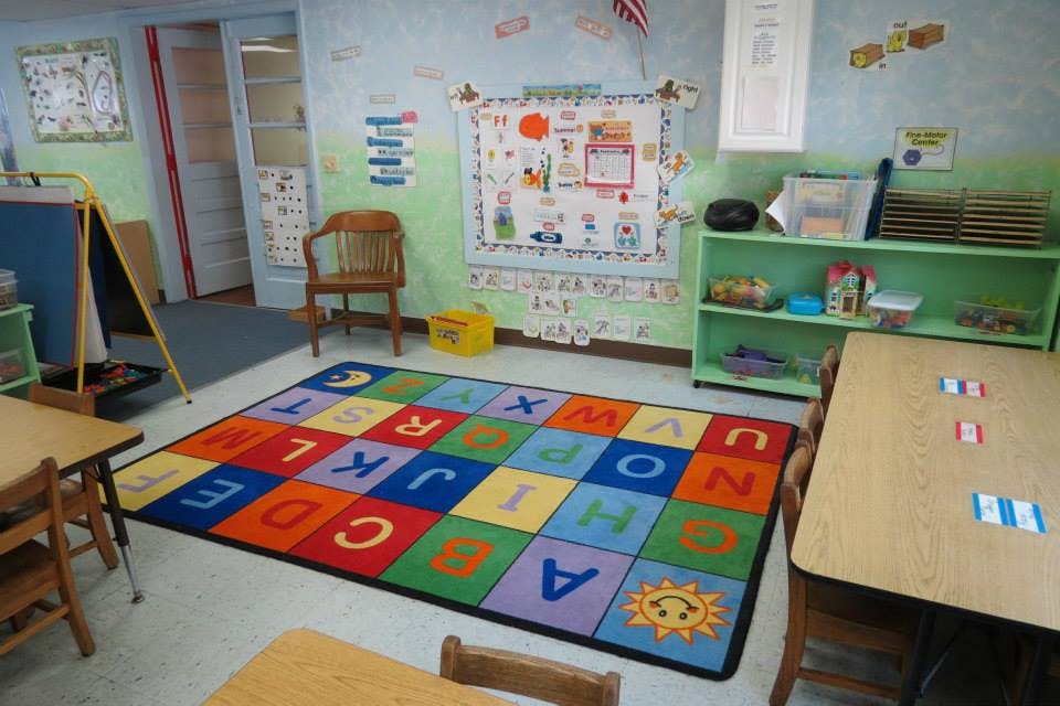 Classroom with an alphabet rug, small tables, and shelves