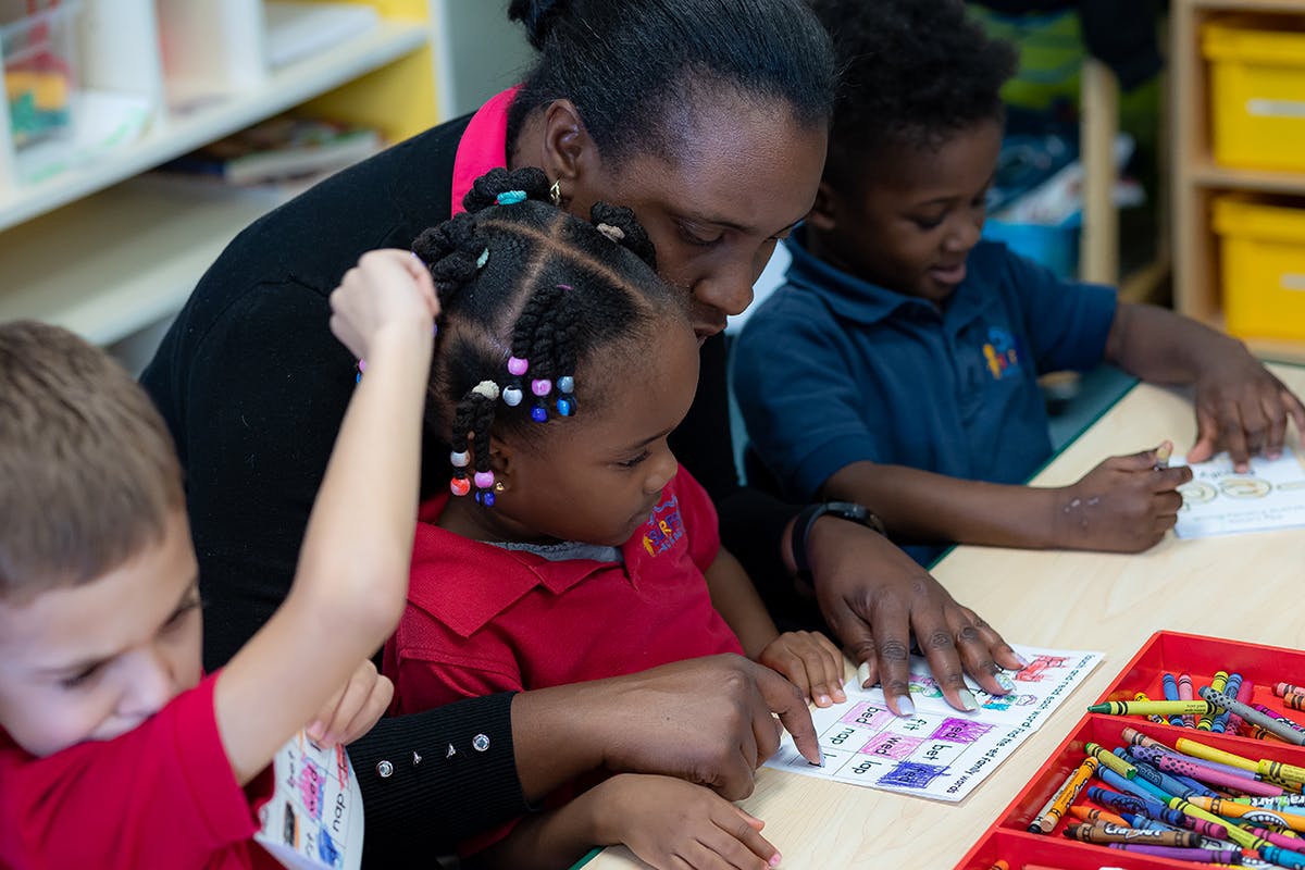 Adult and two children looking at a paper on a table with crayons