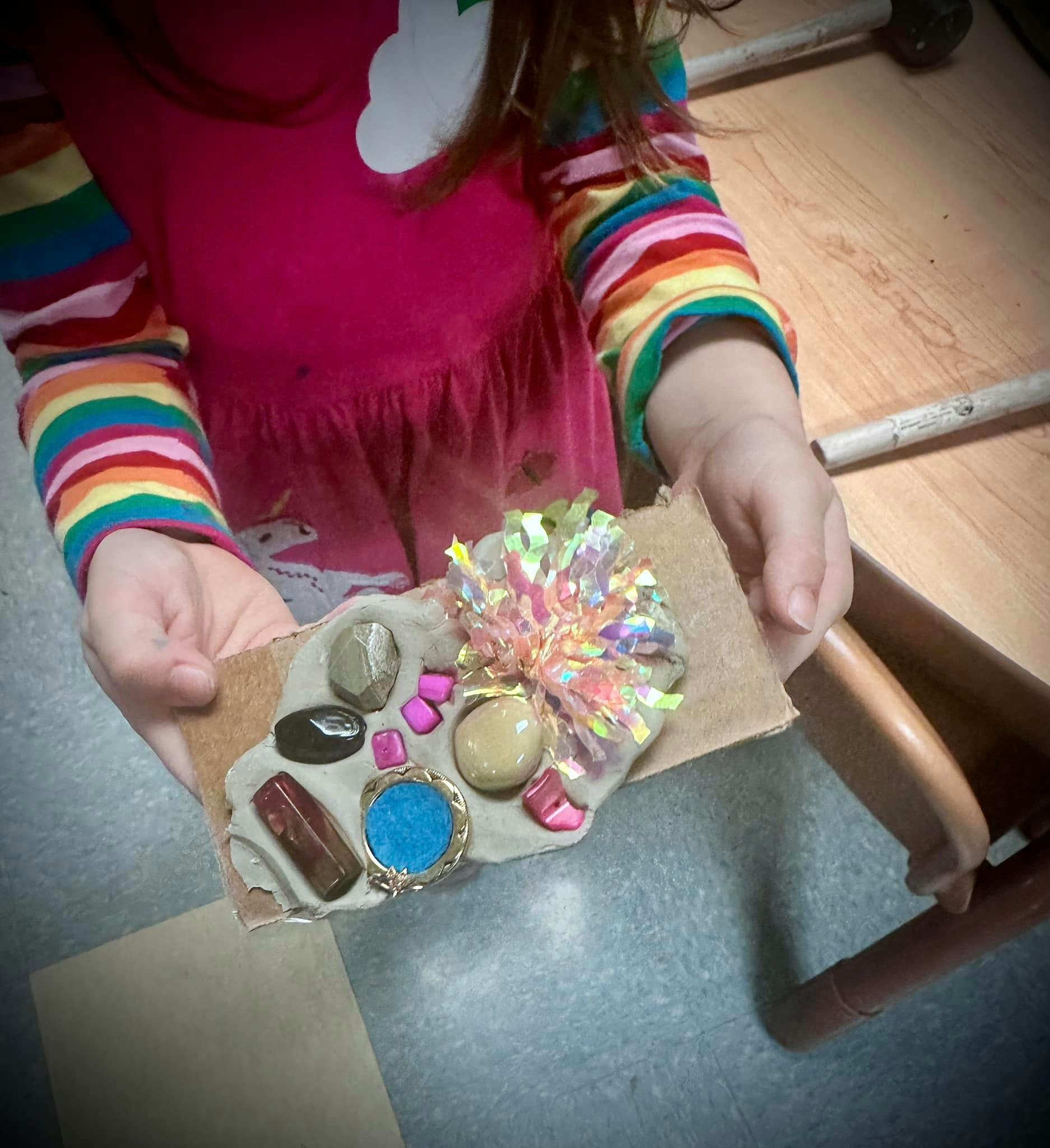 Child holding a decorated craft with stones and a shiny pom-pom