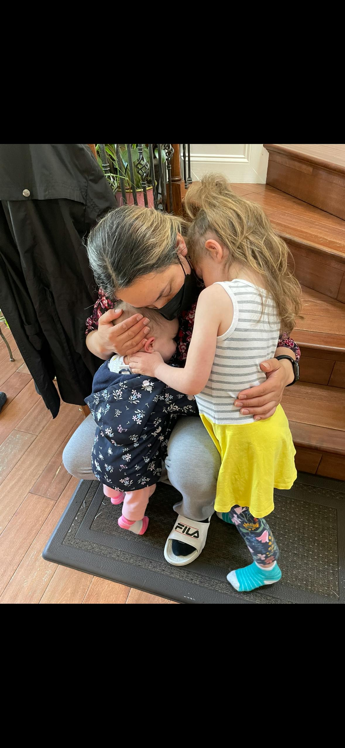 Person holding a child while another child stands next to them