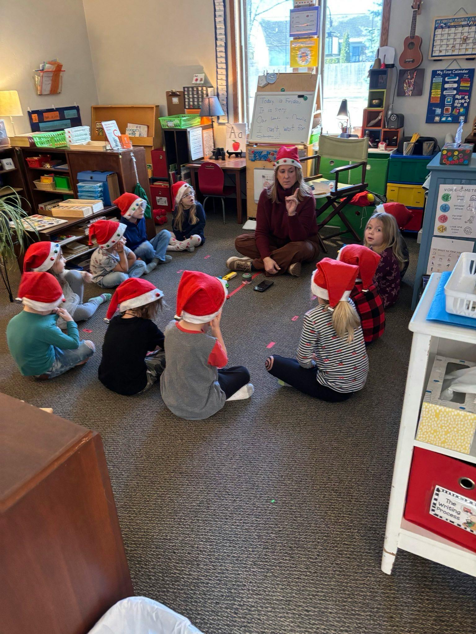 Adult and children in Santa hats sitting on the floor in a classroom