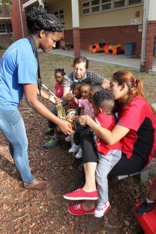 Person holding a saxophone for a group of children and adults