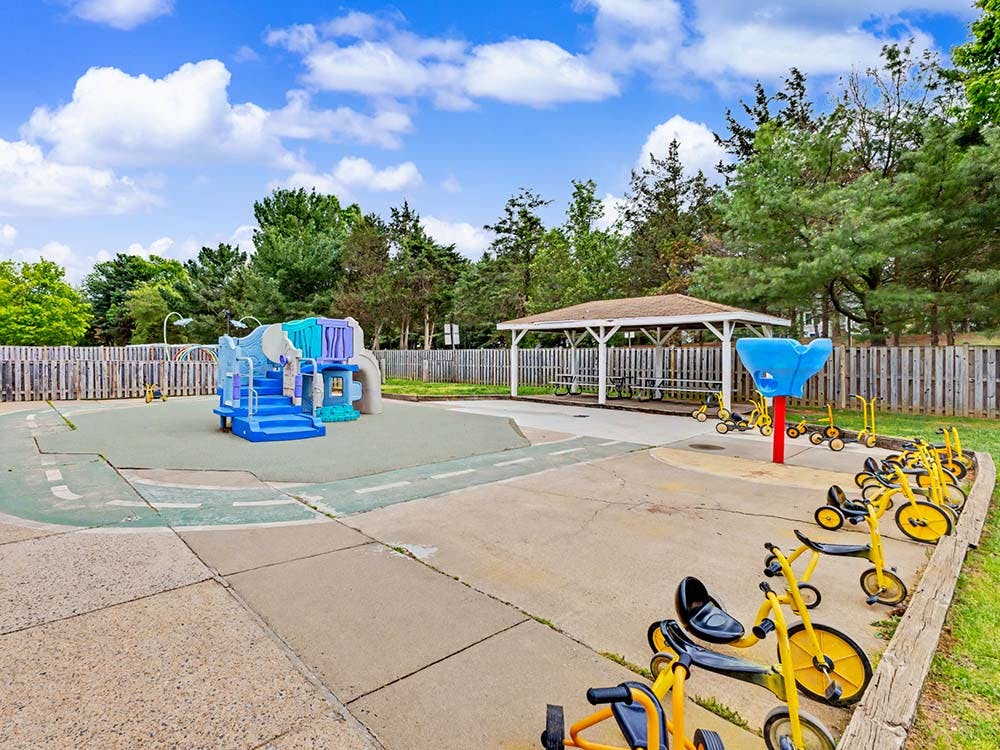 Children's playground with blue play structure, yellow tricycles, and a gazebo