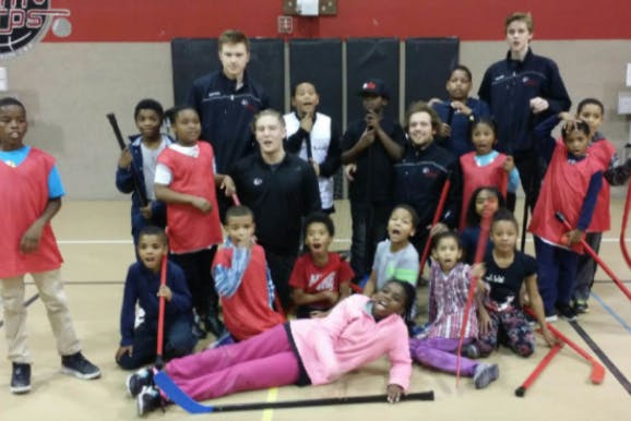 Group of adults and children with hockey sticks in a gym