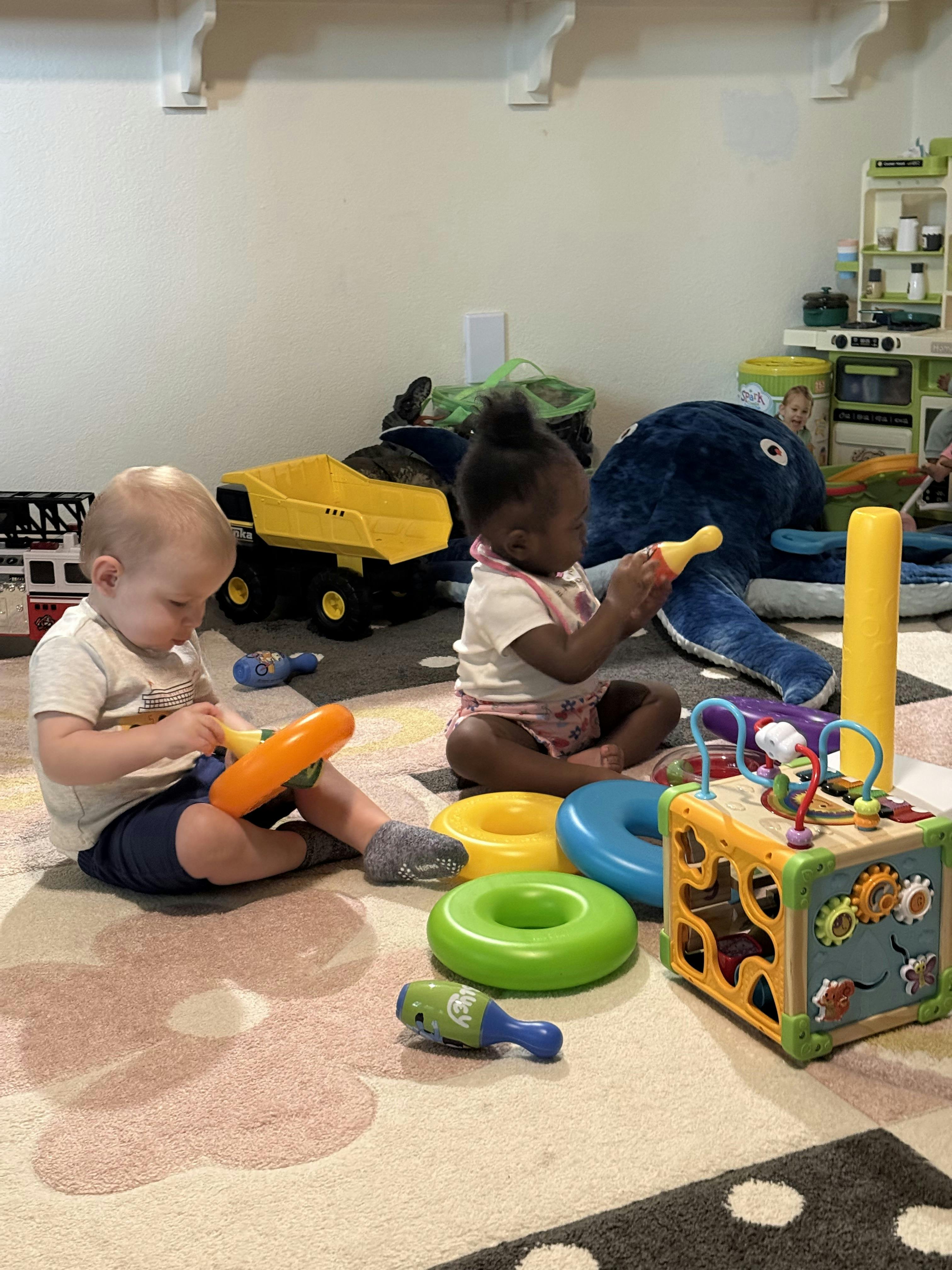 Two children sitting on a rug playing with assorted plastic toys