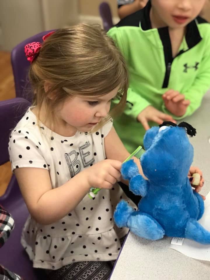 Child brushing the teeth of a blue stuffed animal