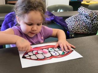 Child brushing teeth on a paper cutout of a mouth