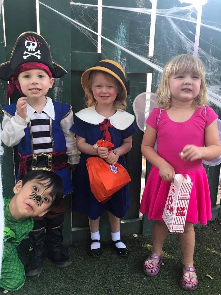 Four children in costumes, one dressed as a pirate, one in a blue dress, one in a pink dress, and one with face paint