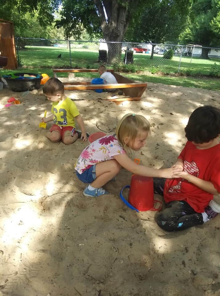 Three children playing in a sandbox with toys
