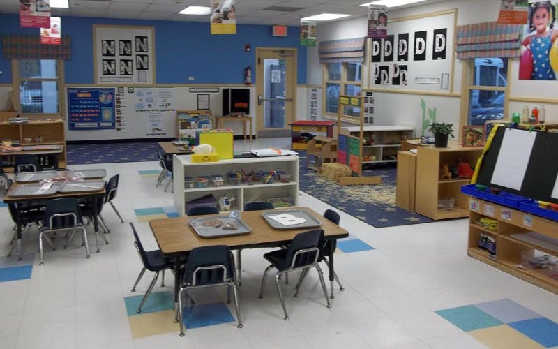Empty classroom with small tables and chairs, shelves with toys, and posters on walls