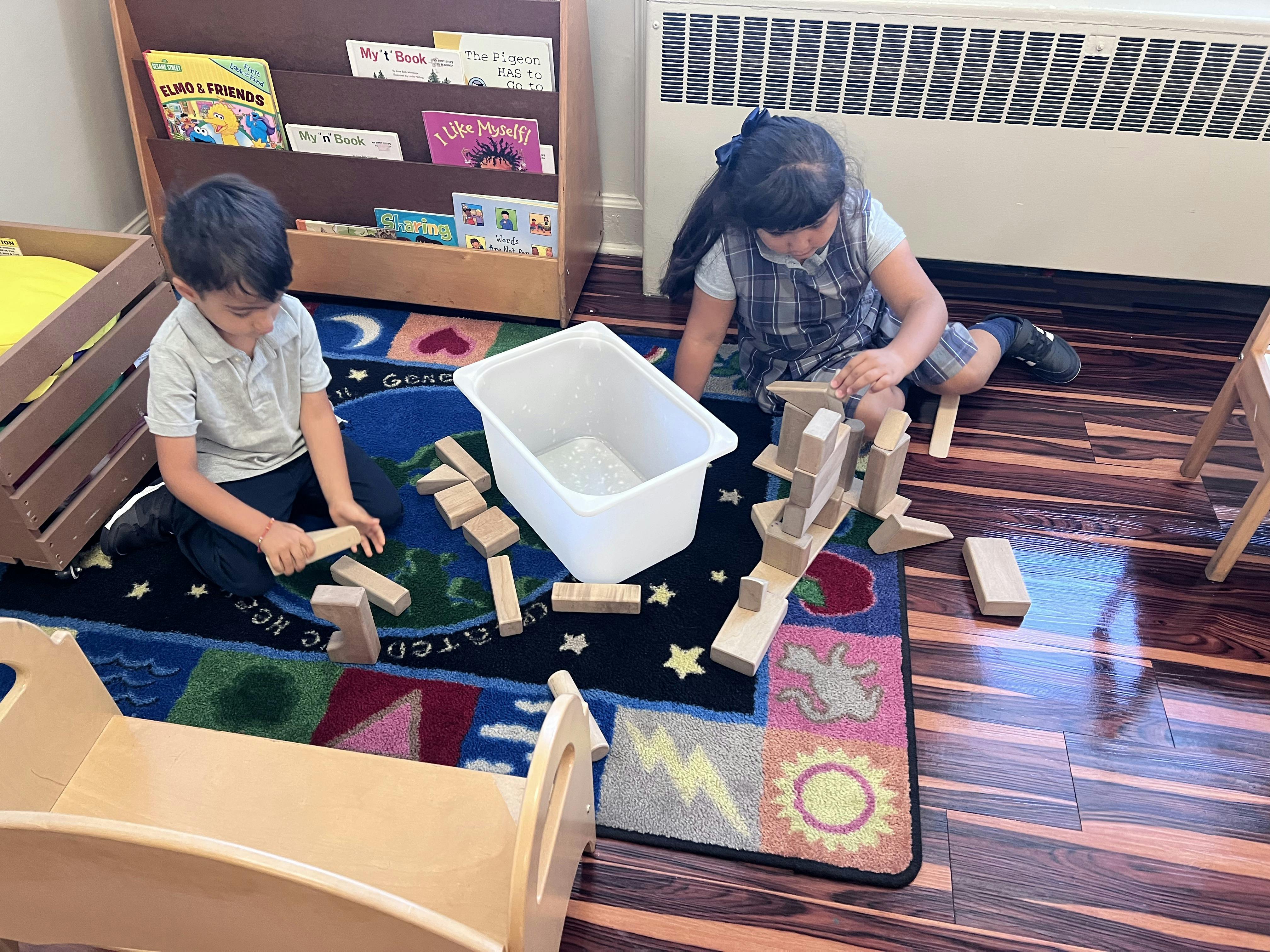 Two children playing with wooden blocks on a rug in a classroom