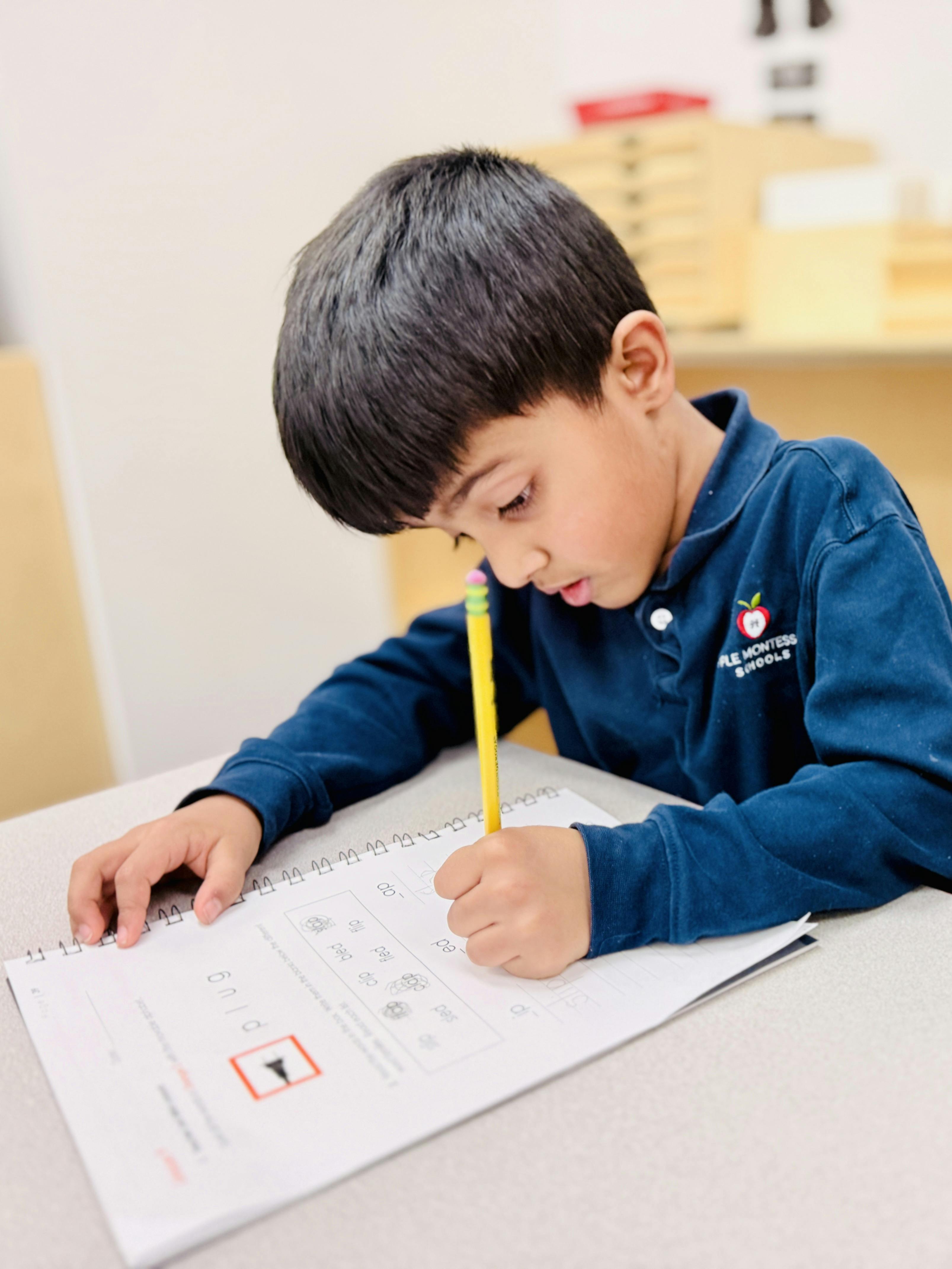 Child writing with a pencil in a notebook on a desk