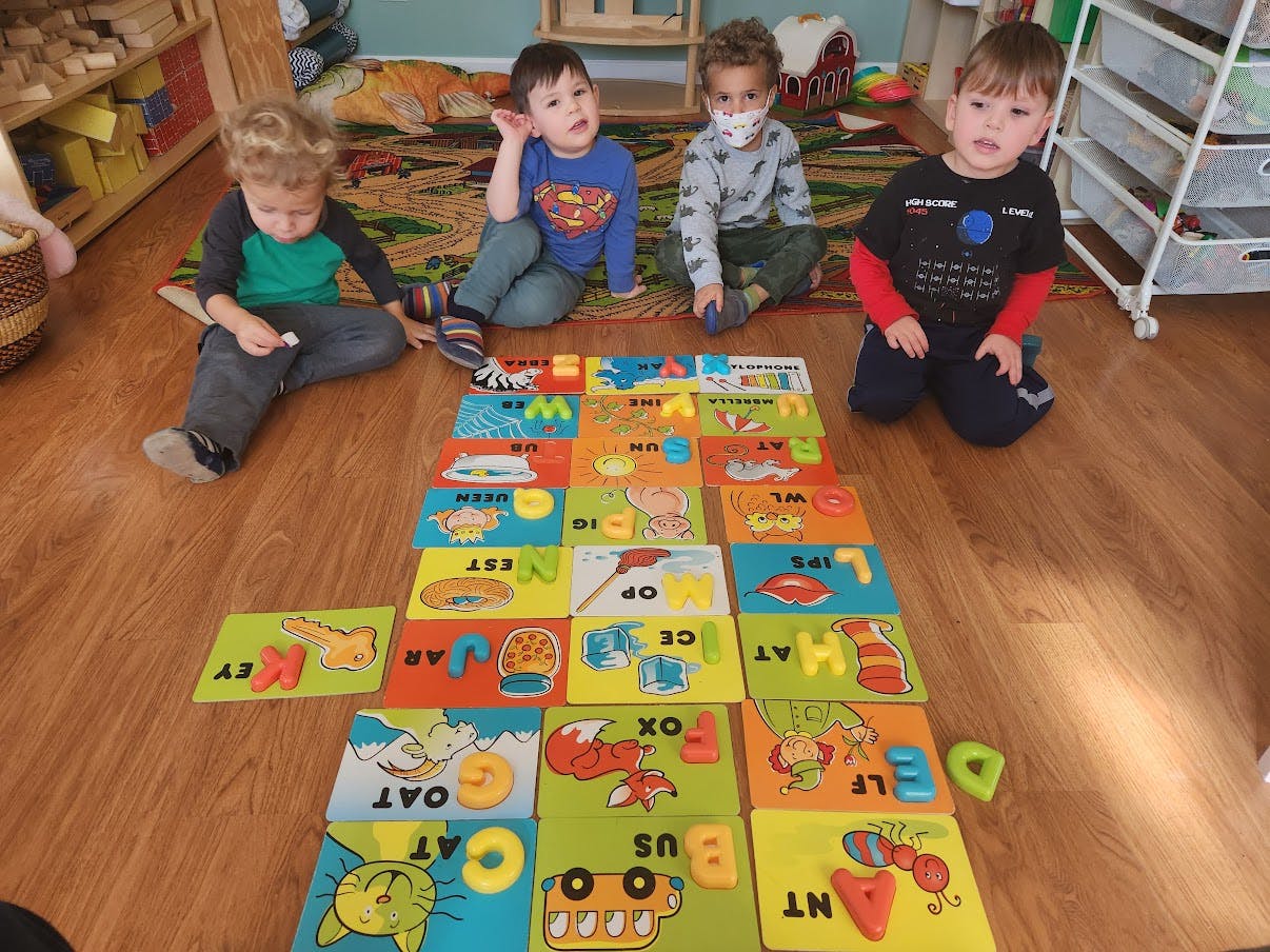 Four children playing with alphabet puzzle pieces on a wooden floor