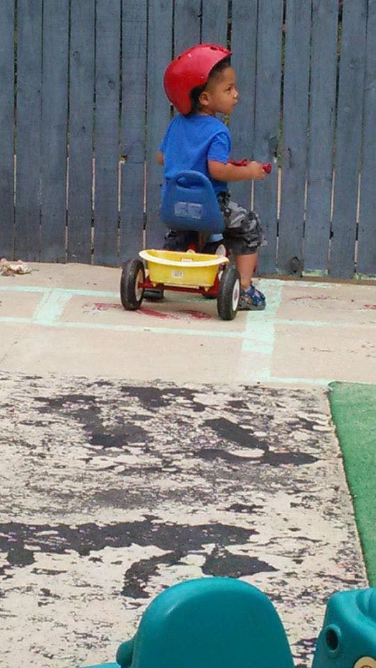 Child in a red helmet riding a yellow wagon