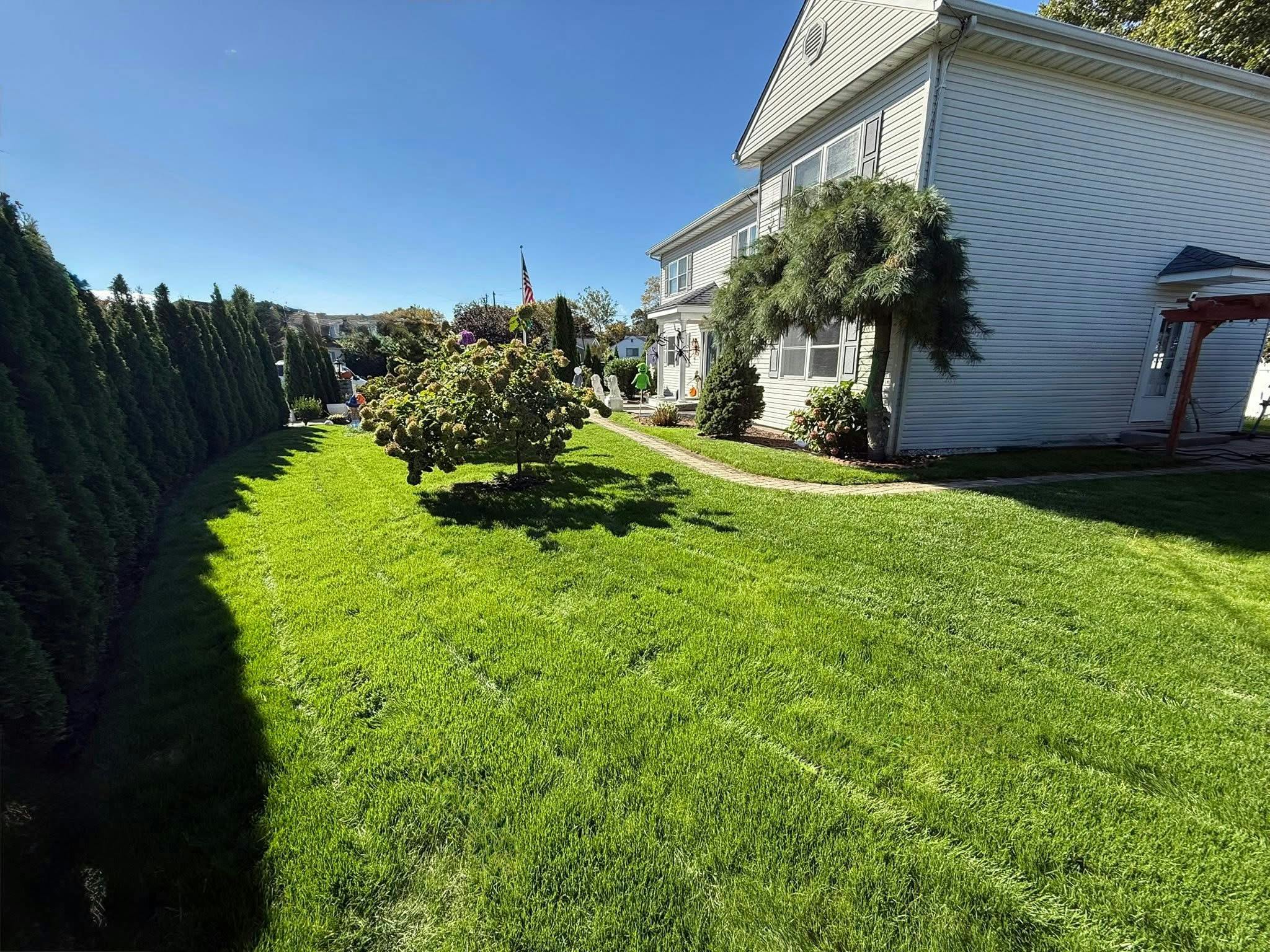 Side view of a white house with green lawn, path, and hedges
