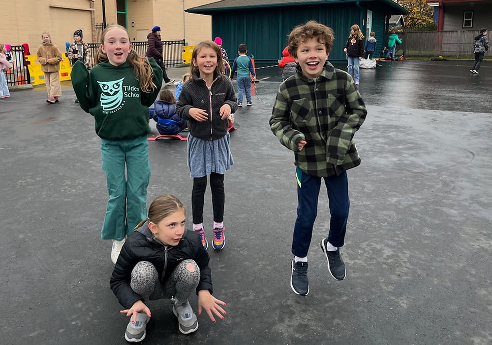 Four children playing outdoors, two jumping in the air and one crouching