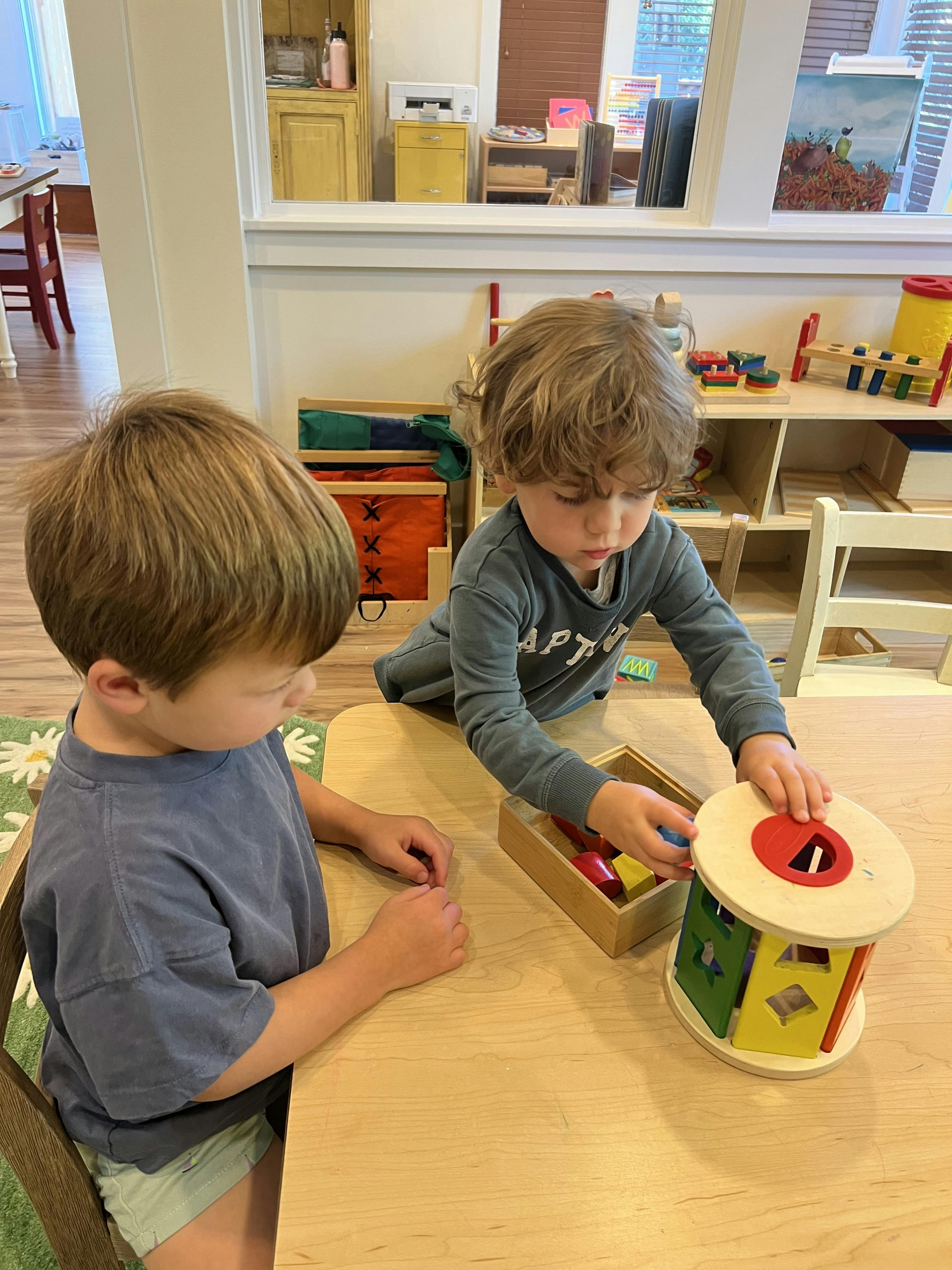 Two children playing with toys at a table in a classroom