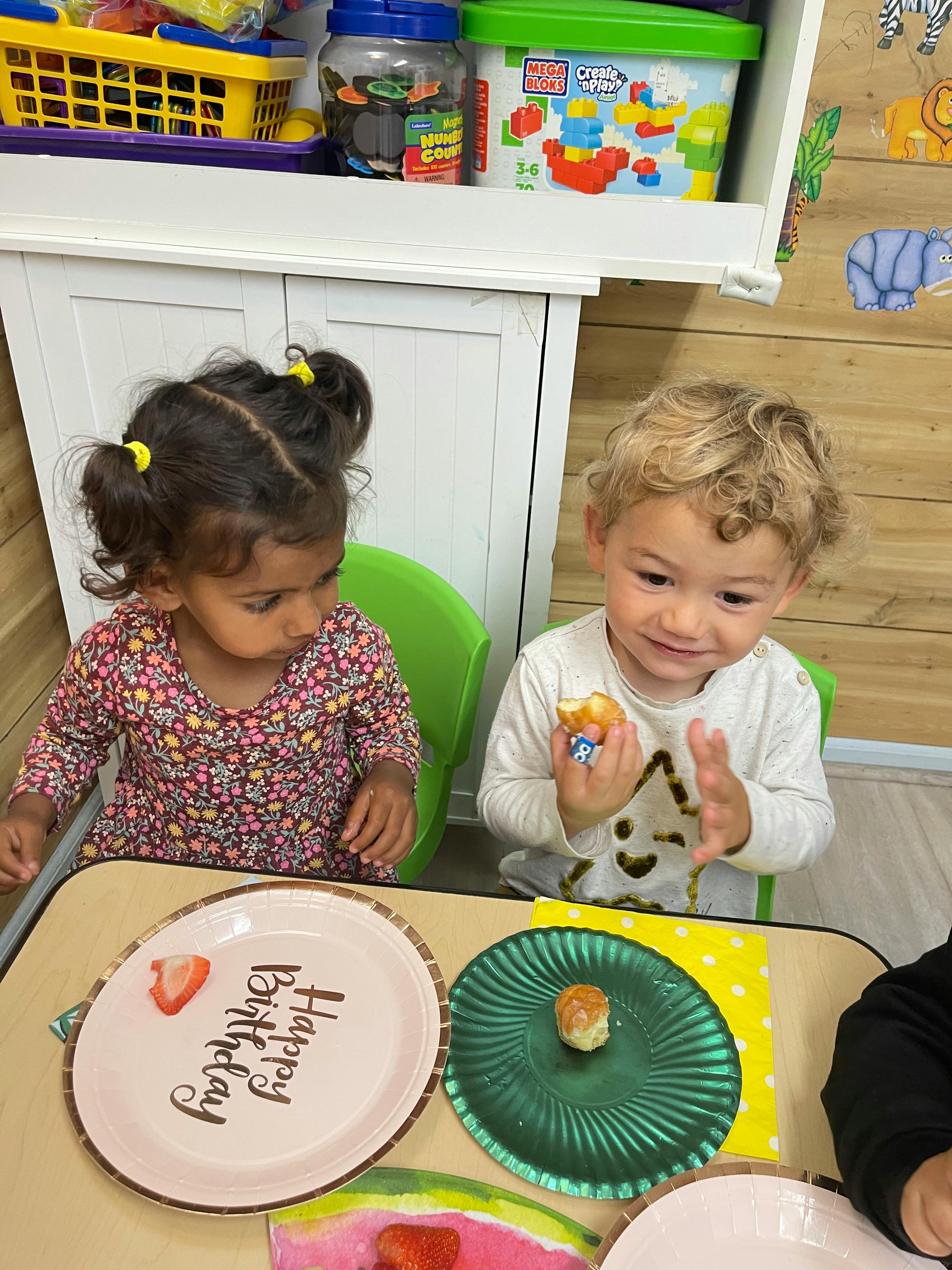 Two children sitting at a table with plates, one with "Happy Birthday" text
