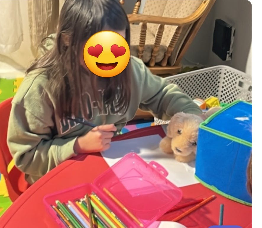 Child drawing at a table with a toy dog nearby