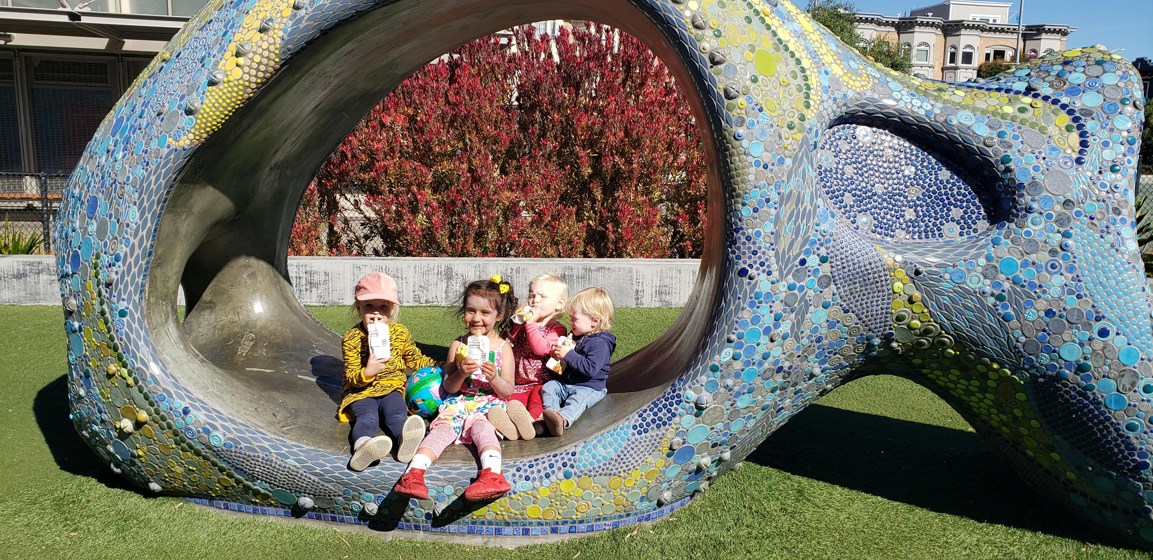 Four children sitting inside a large, colorful, mosaic sculpture
