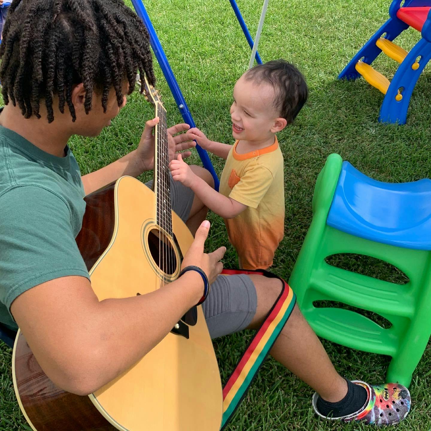 Person playing guitar for a child outdoors