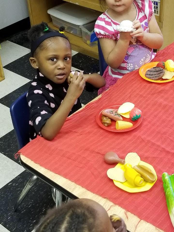 Child sitting at a table with play food