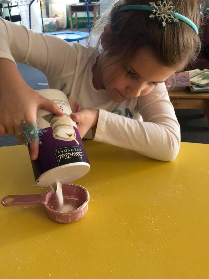 Child pouring liquid from a container into a measuring cup