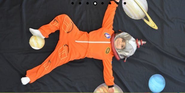 Child in astronaut costume lying on black fabric with planet models