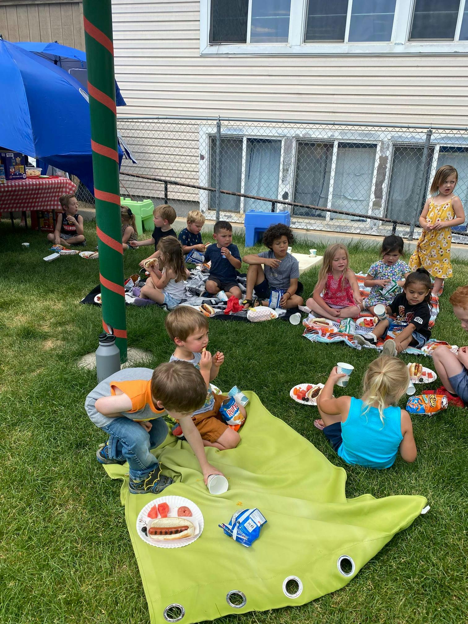 Children sitting on blankets on grass, eating food
