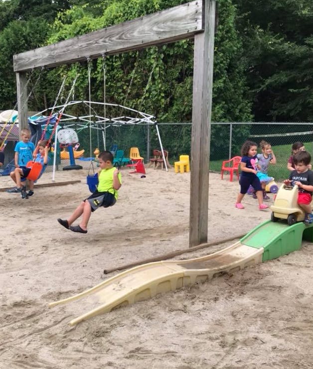 Children playing on swings and a slide in a sandy playground