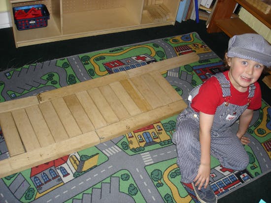 Child in overalls and cap kneeling on a playmat next to wooden blocks