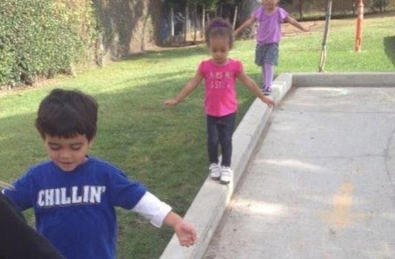 Three children balancing on a low concrete wall