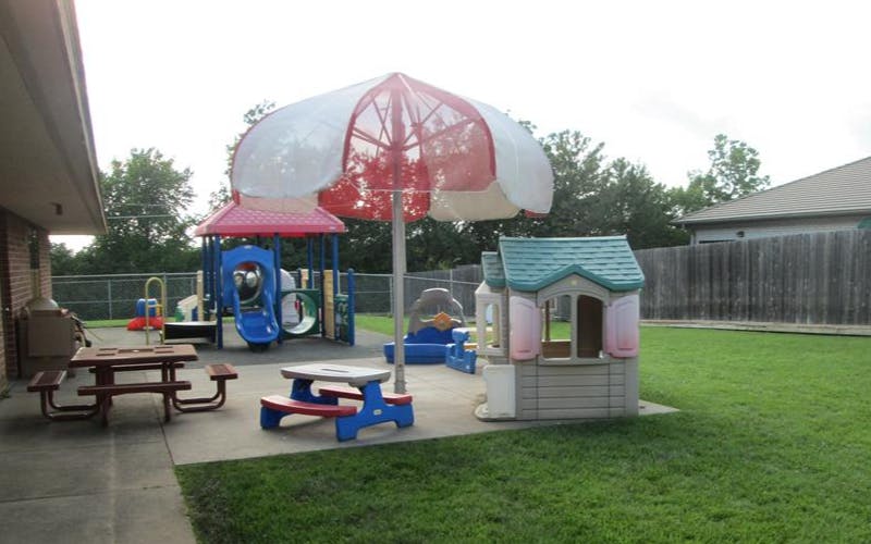 Outdoor playground with slides, playhouse, picnic tables, and umbrella