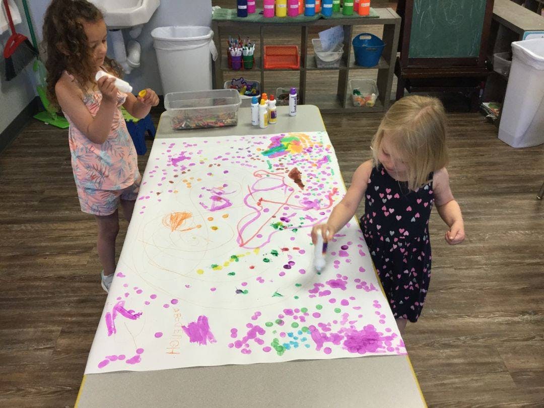 Two children painting on a large sheet of paper on a table