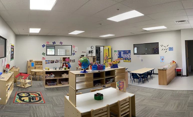 Empty classroom with small tables, chairs, and shelves with learning materials