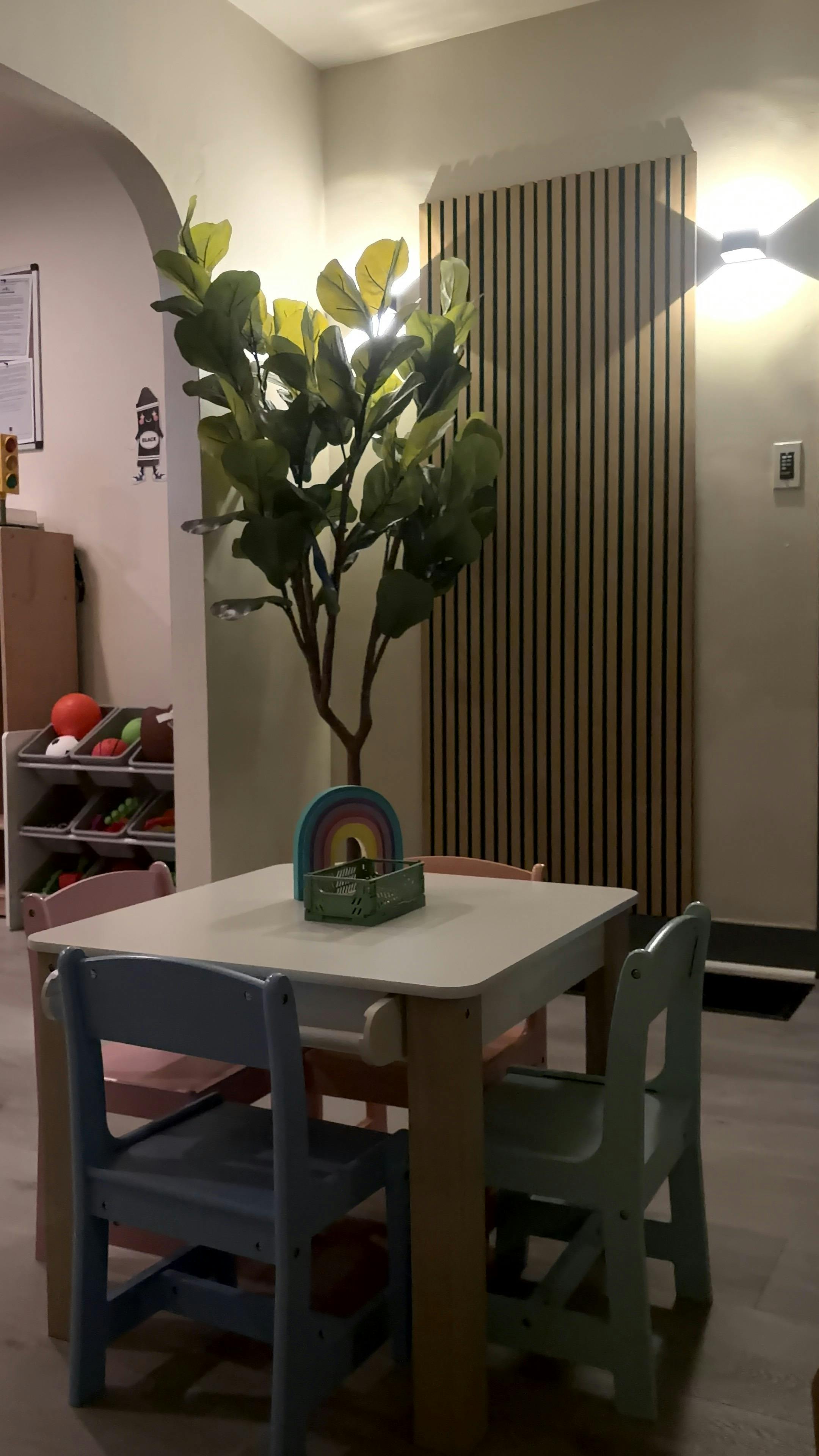 Small table with three chairs, a plant, and a rainbow toy in a room