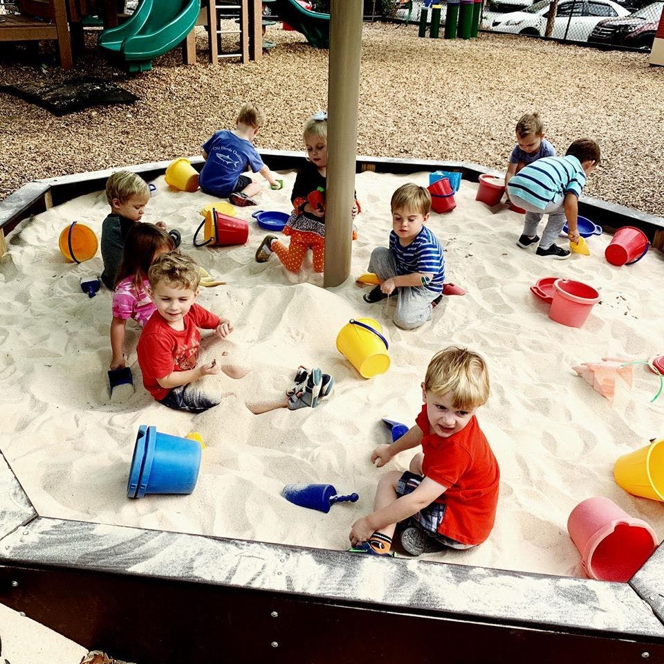 Children playing in a large sandbox with toys