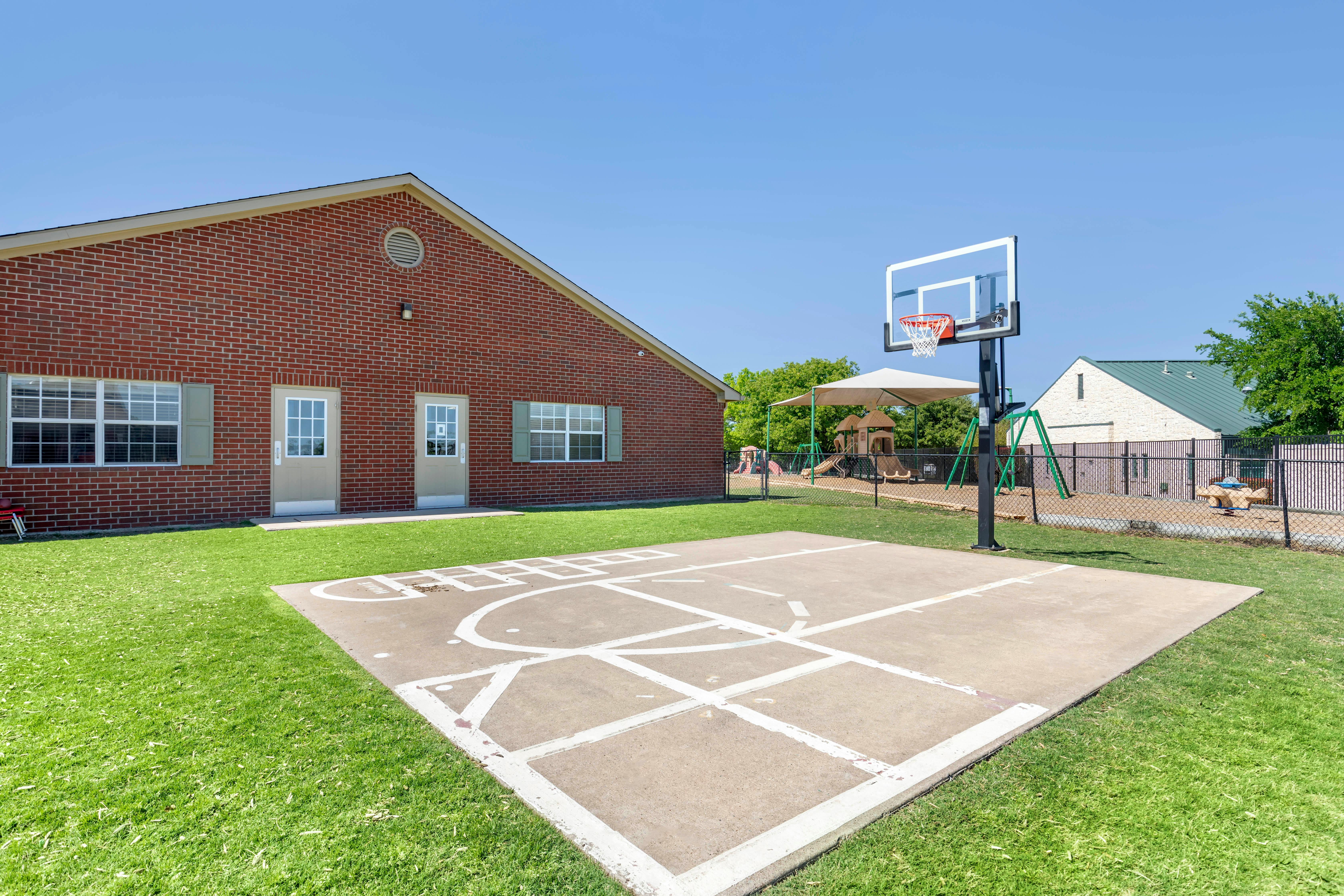 Brick building with a basketball hoop, green grass, and playground equipment
