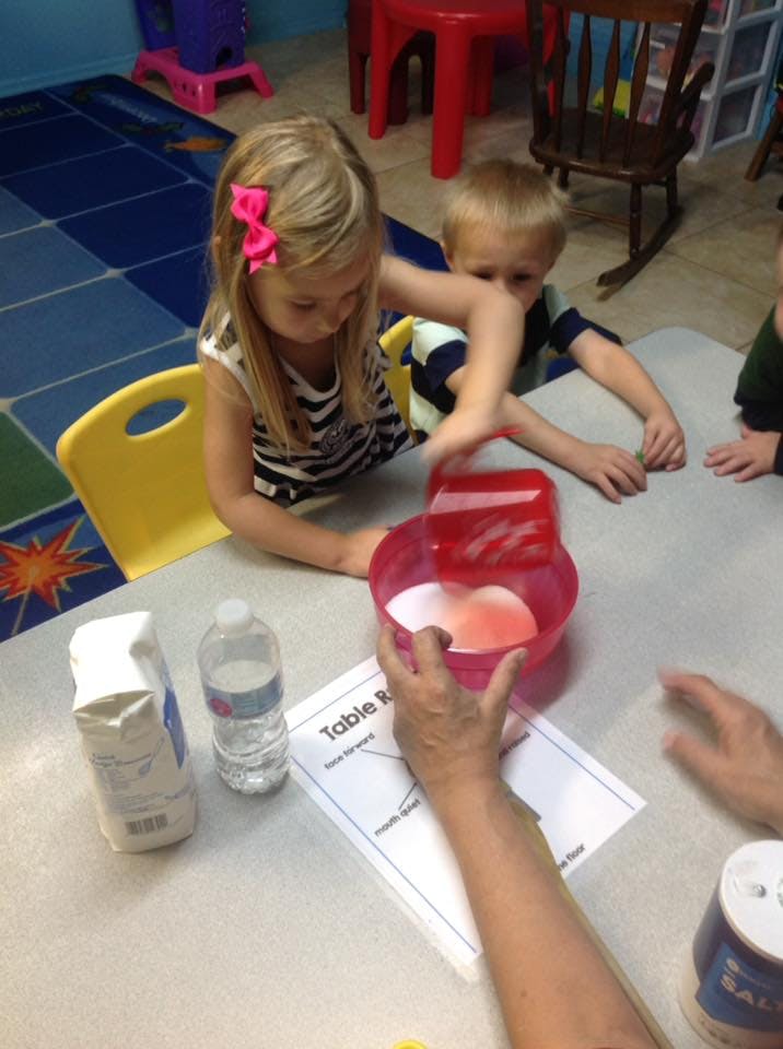Child mixing ingredients in a bowl with an adult's hand assisting