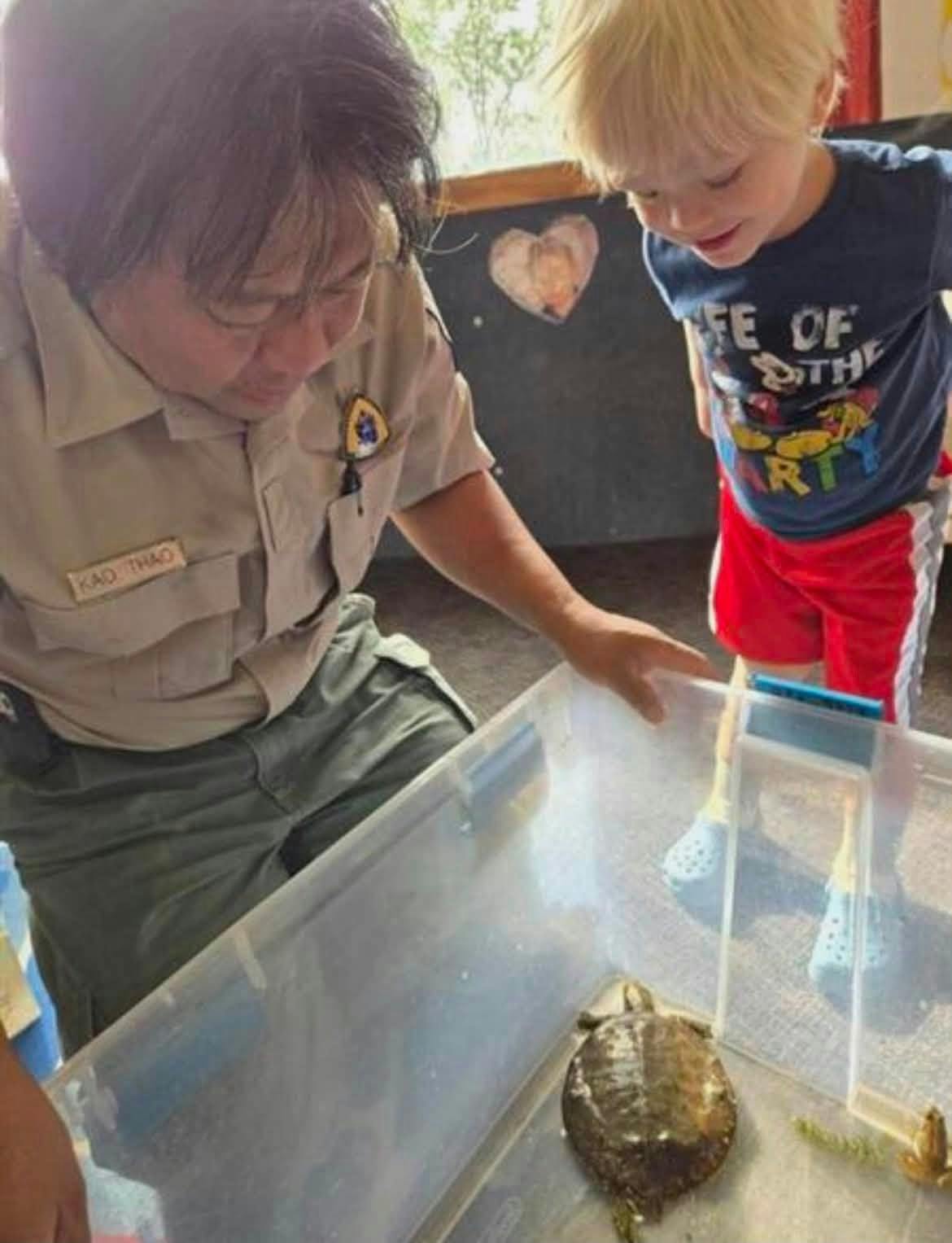 Person in uniform showing a turtle in a container to a child