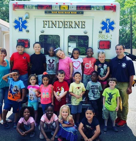 Group of children and two adults posing in front of an ambulance