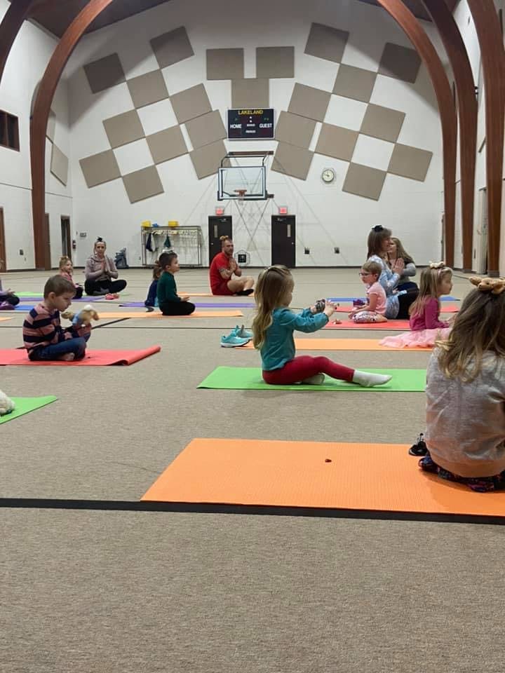 Children and adults sitting on yoga mats in a large room