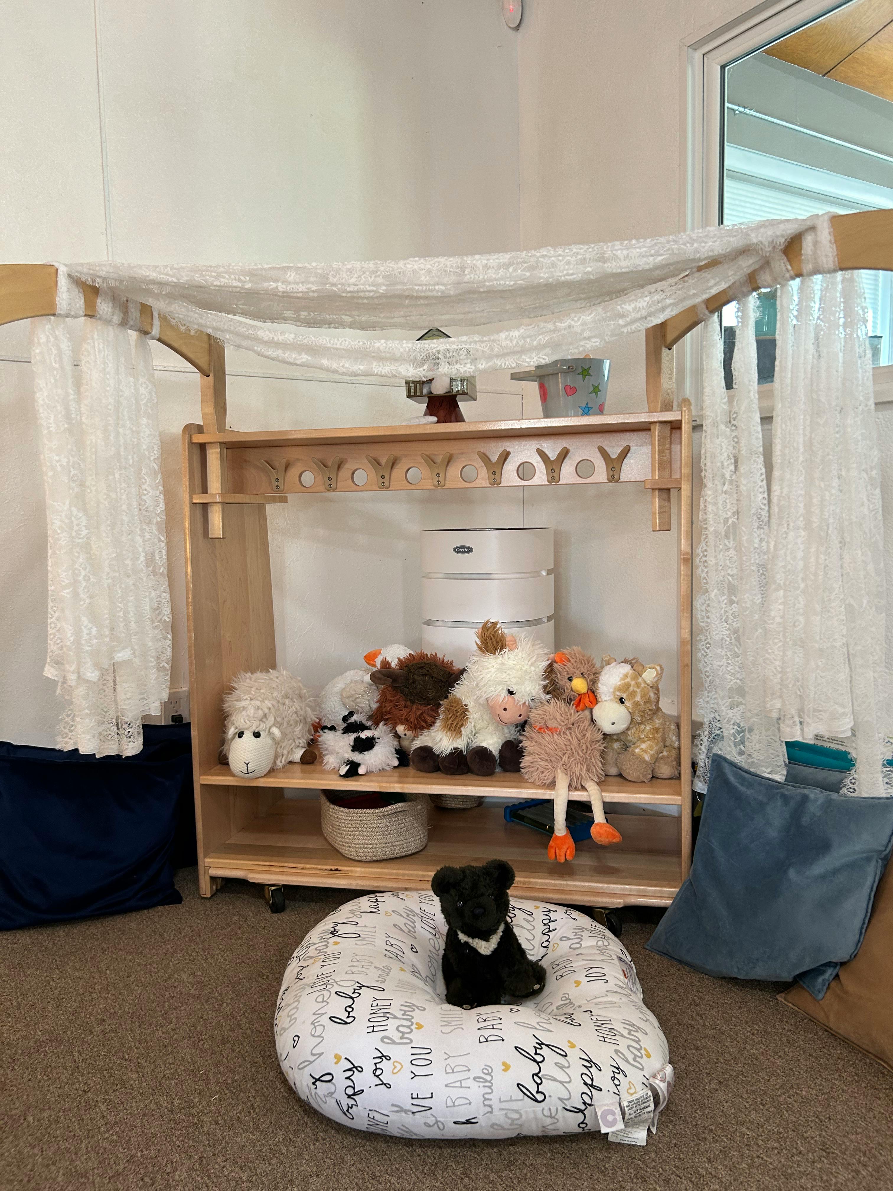 Black stuffed animal on a white pillow in front of a shelf with toys